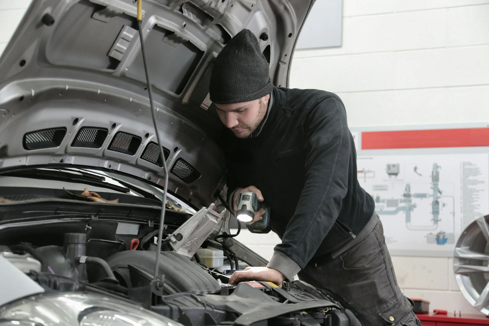 A man repairs a car in a garage, surrounded by tools and equipment, focused on his work.