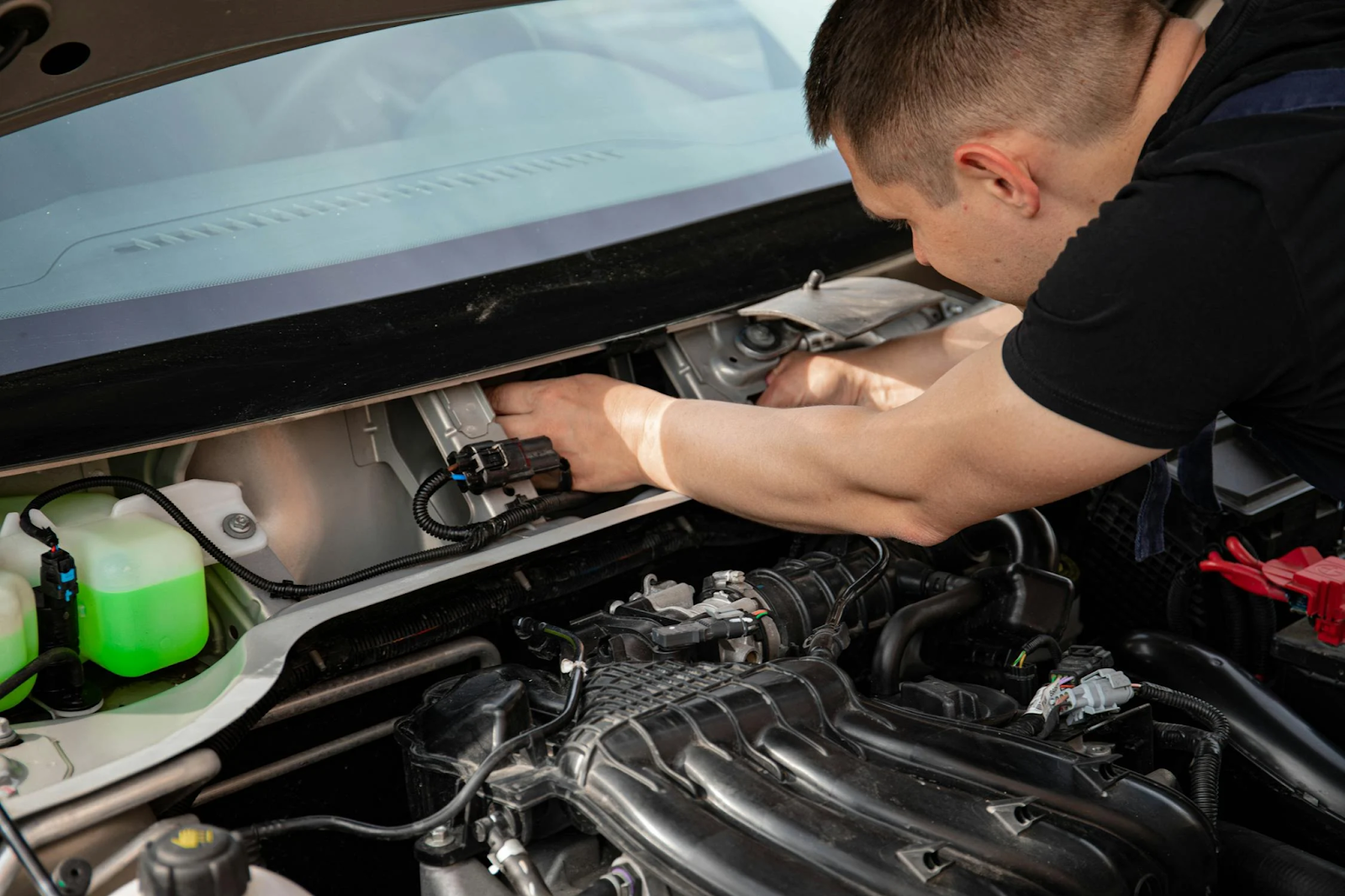 A man repairs a car in a garage, surrounded by tools and equipment, focused on his work.